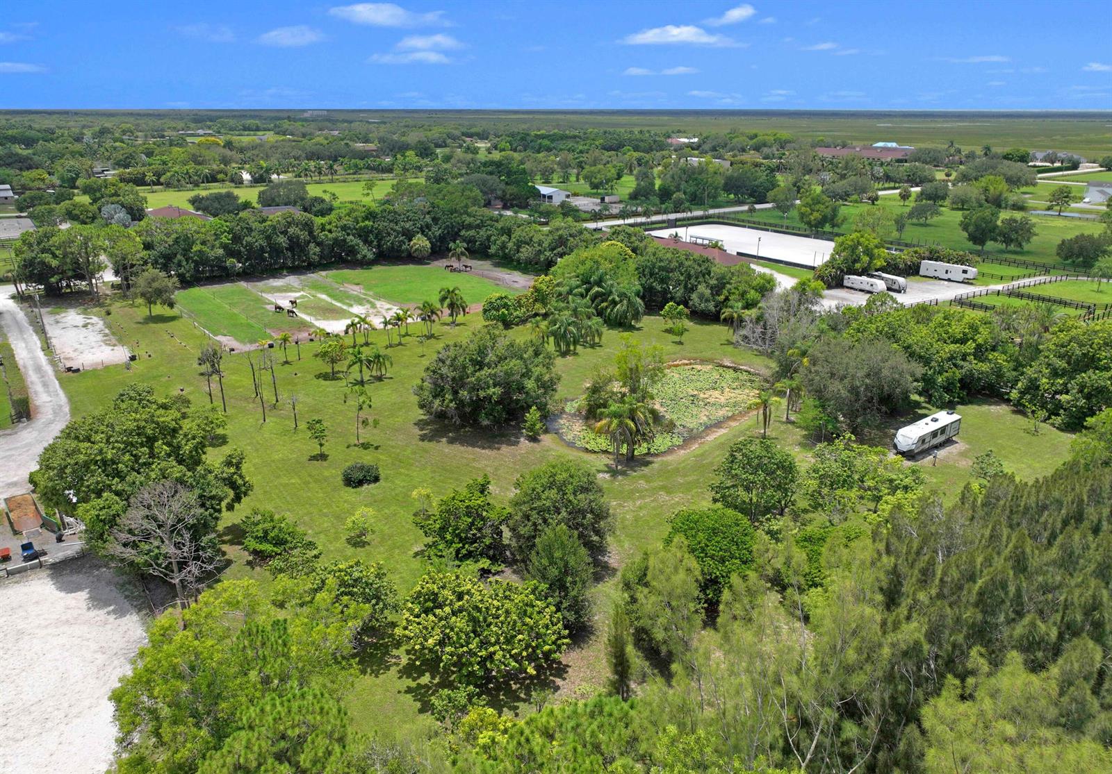 An aerial view shows a grassy property with a pond, trees, and parked recreational vehicles — 16639 Hollow Tree Lane, Wellington FL 33470, WELLINGTON, FL