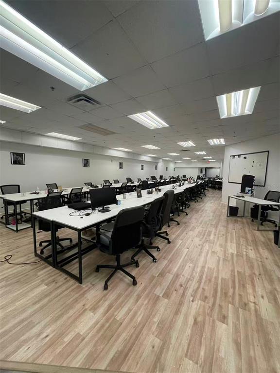 A long, open-plan office space features rows of desks, rolling chairs, and light wood flooring — 7075 KINGSPOINTE PARKWAY UNIT 9, ORLANDO, FL