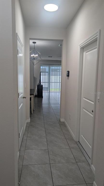 A hallway with gray tile flooring leads to an open living area with a chandelier — 4015 BLUE BANKS LANE, BRADENTON, FL