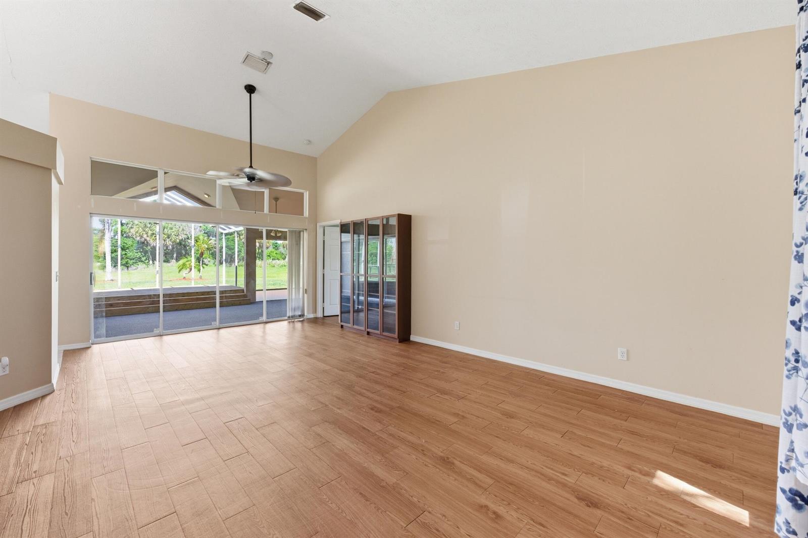 A spacious living room with vaulted ceilings, wood-look tile flooring, and sliding glass patio doors — 1960 SE 9th Avenue, Okeechobee FL 34974, OKEECHOBEE, FL