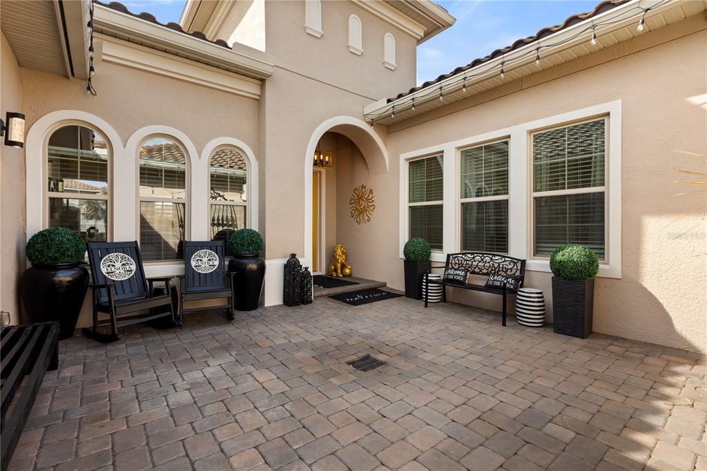 A paved courtyard features arched windows, two rocking chairs, a bench, and potted topiary plants — 3880 GRASSLAND LOOP, LAKE MARY, FL