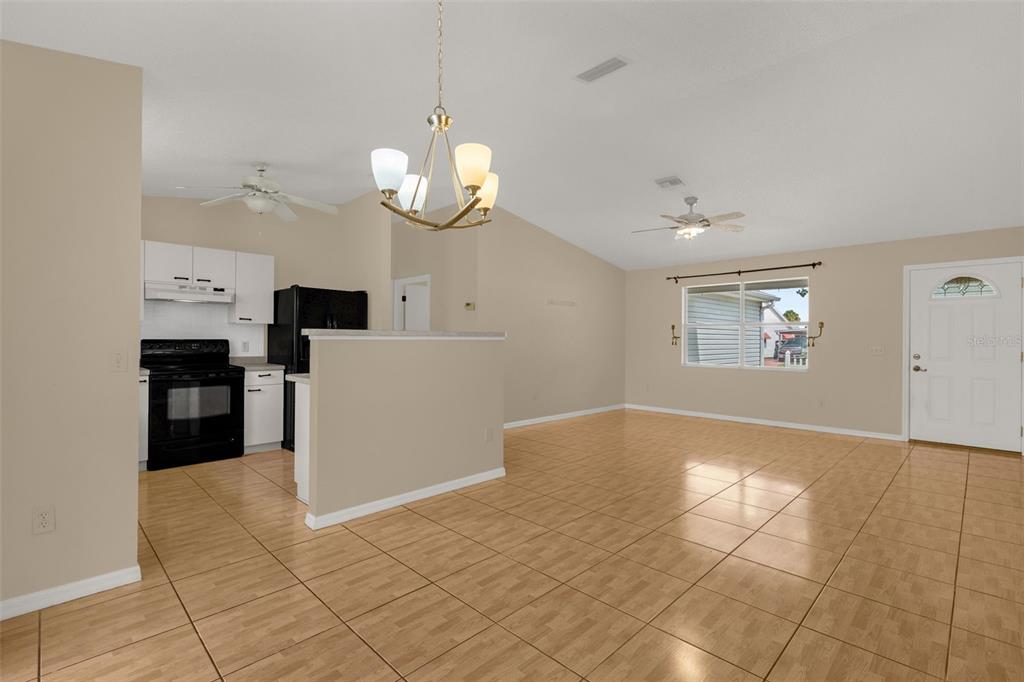 An open-concept living area features light-colored tile flooring, a kitchen with black appliances, and vaulted ceilings — 1222 GRANADA COURT, THE VILLAGES, FL