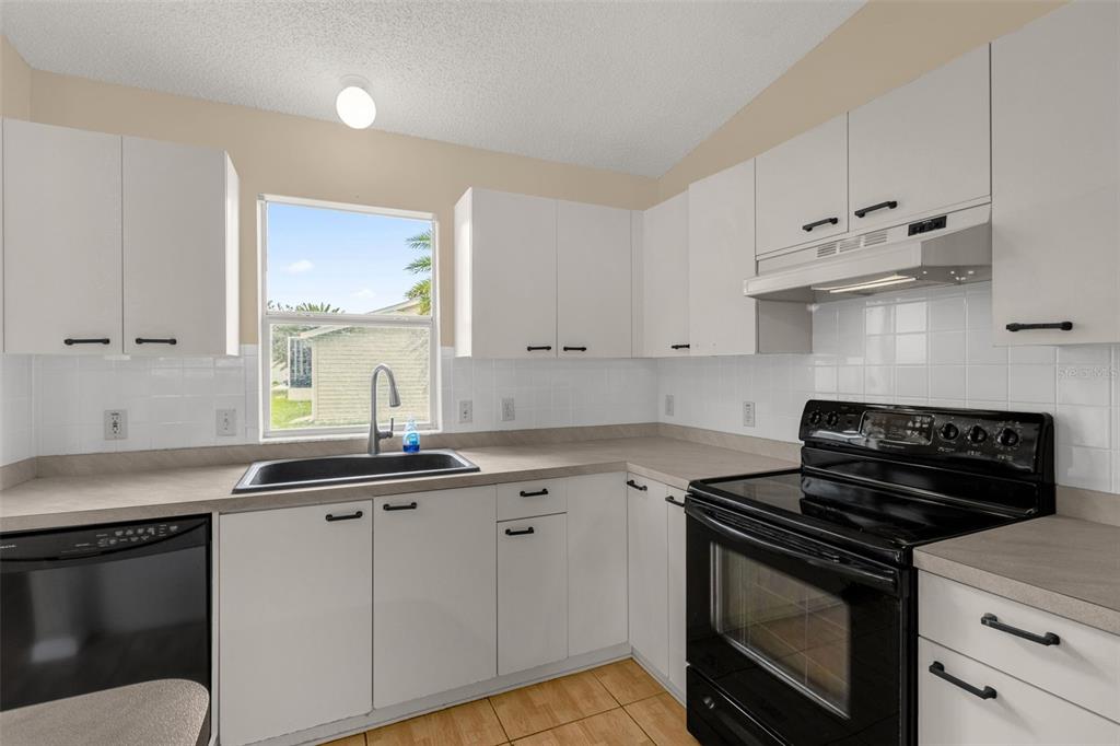 A kitchen with white cabinets, light countertops, a black dishwasher, and a black electric range — 1222 GRANADA COURT, THE VILLAGES, FL