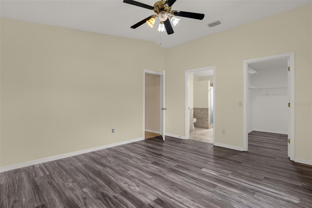 A bedroom with light walls, wood-look flooring, a ceiling fan, and two open doorways — 1222 GRANADA COURT, THE VILLAGES, FL