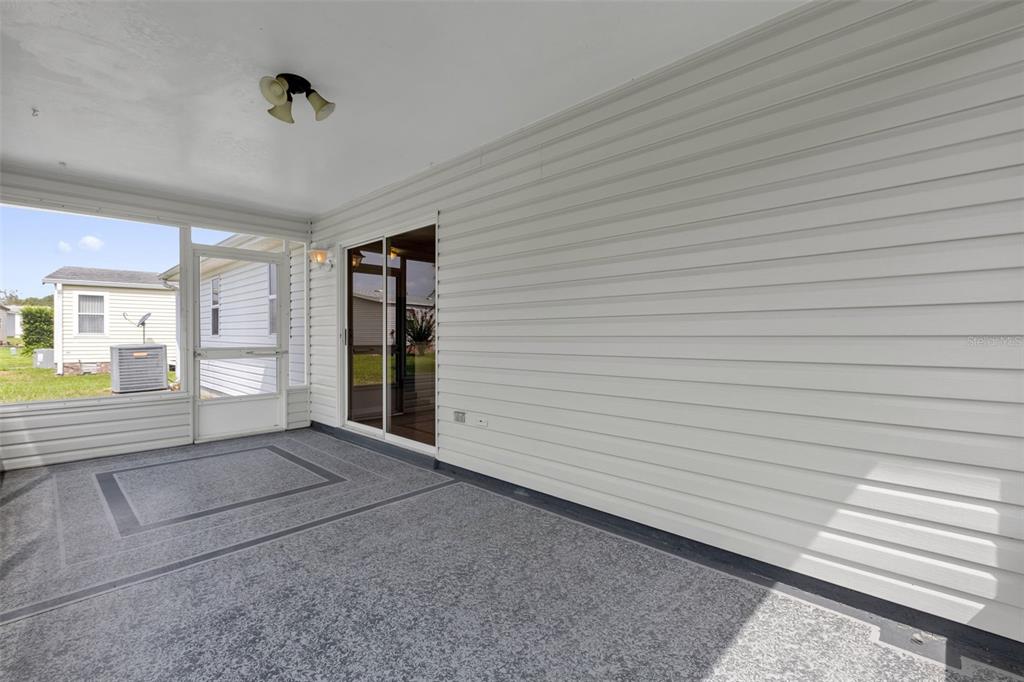 A covered patio features a speckled concrete floor, white vinyl siding, and a sliding glass door — 1222 GRANADA COURT, THE VILLAGES, FL