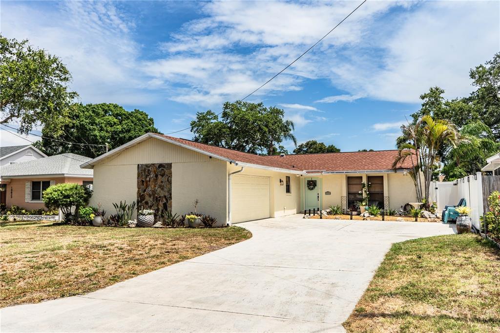 A single-story house with a beige exterior, stone accent wall, and a concrete driveway — 14803 SUNSET DRIVE, LARGO, FL