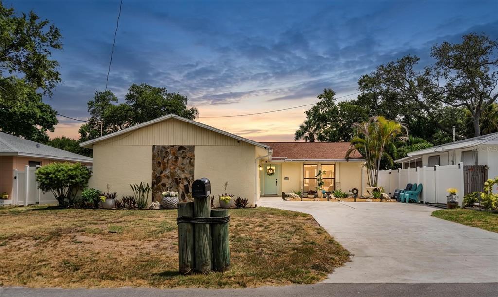 A single-story house with a stone accent wall, light-colored siding, and a concrete driveway — 14803 SUNSET DRIVE, LARGO, FL