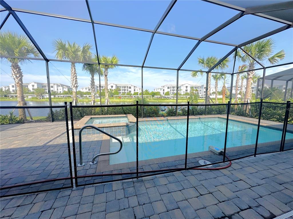 A screened-in swimming pool and spa overlook a lake with palm trees in the background — 25018 LONG MEADOW DRIVE, PUNTA GORDA, FL