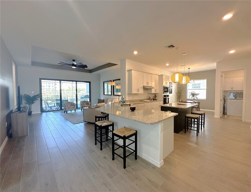 An open-concept kitchen and living area features light tile flooring, granite countertops, and sliding doors — 25018 LONG MEADOW DRIVE, PUNTA GORDA, FL