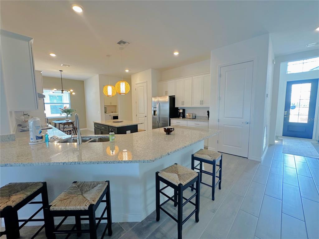 A kitchen features white cabinetry, granite countertops, a center island, and bar stools — 25018 LONG MEADOW DRIVE, PUNTA GORDA, FL