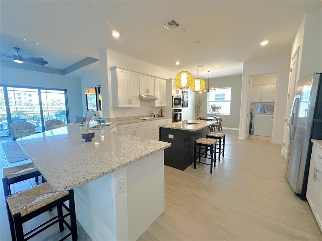 A kitchen features white cabinets, granite countertops, a dark island, and light wood-look tile flooring — 25018 LONG MEADOW DRIVE, PUNTA GORDA, FL