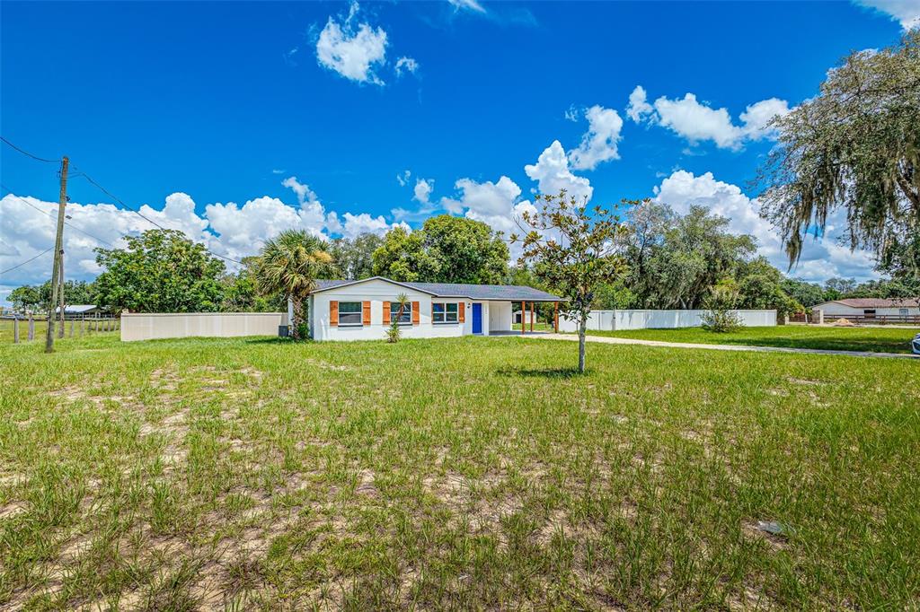 A white single-story house with a blue front door sits on a large grassy lot — 4994 E HINSON AVENUE, HAINES CITY, FL