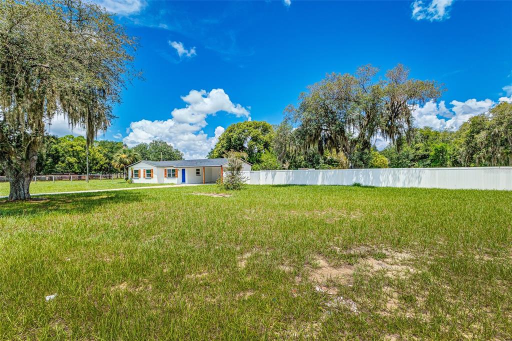 A white single-story house sits behind a large grassy yard and a white privacy fence — 4994 E HINSON AVENUE, HAINES CITY, FL