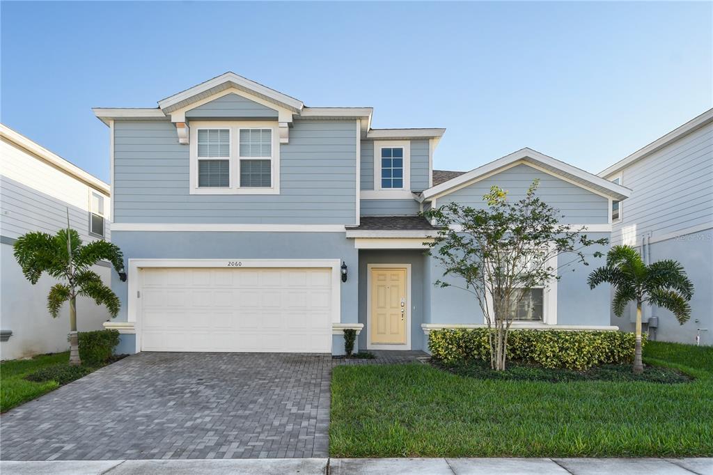 A two-story light blue house features a two-car garage, a yellow door, and palm trees — 2060 LELANI CIR, DAVENPORT, FL