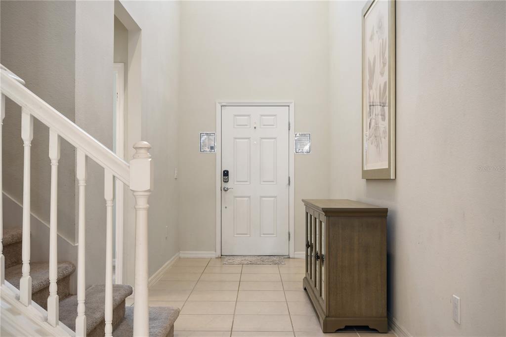 A bright entryway features a high ceiling, a staircase with white railings, and tile flooring — 2060 LELANI CIR, DAVENPORT, FL