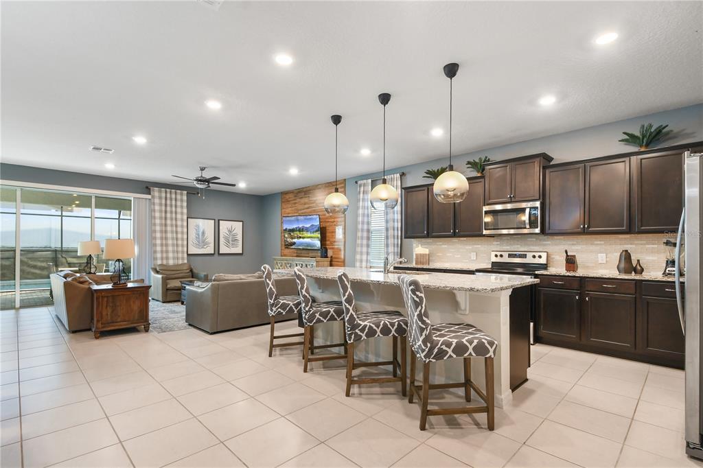An open-concept kitchen and living area features dark wood cabinets, granite countertops, and tile flooring — 2060 LELANI CIR, DAVENPORT, FL