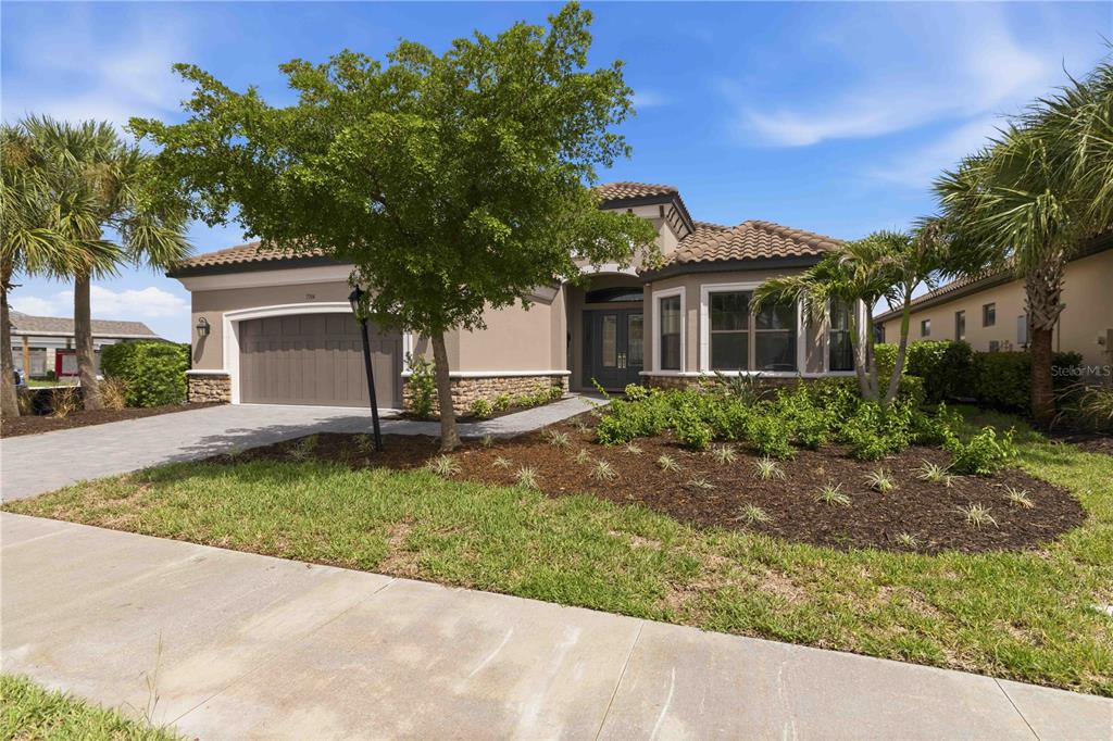 A single-story house with a tile roof, tan stucco exterior, and a landscaped front yard — 7704 MOONBEAM AVENUE, SARASOTA, FL