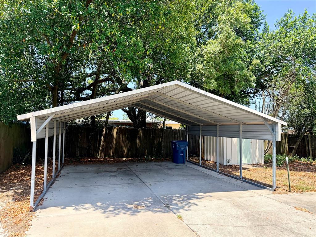 A metal carport stands over a concrete driveway in front of a wooden fence — 7055 MERRICK LANE, SPRING HILL, FL