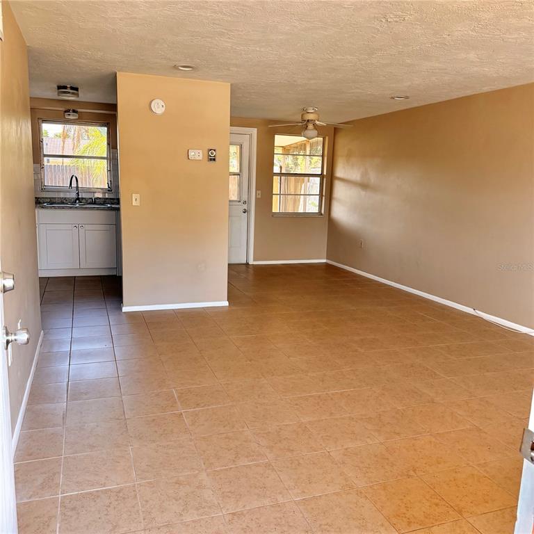 An open-concept living area with tan walls, tile flooring, and an adjacent kitchen — 5401 PASADENA DRIVE, NEW PORT RICHEY, FL