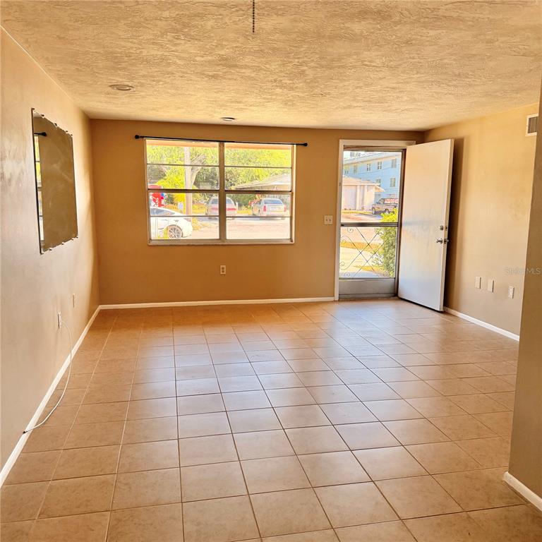 An empty room with tan walls, tiled flooring, a large window, and an open door — 5401 PASADENA DRIVE, NEW PORT RICHEY, FL
