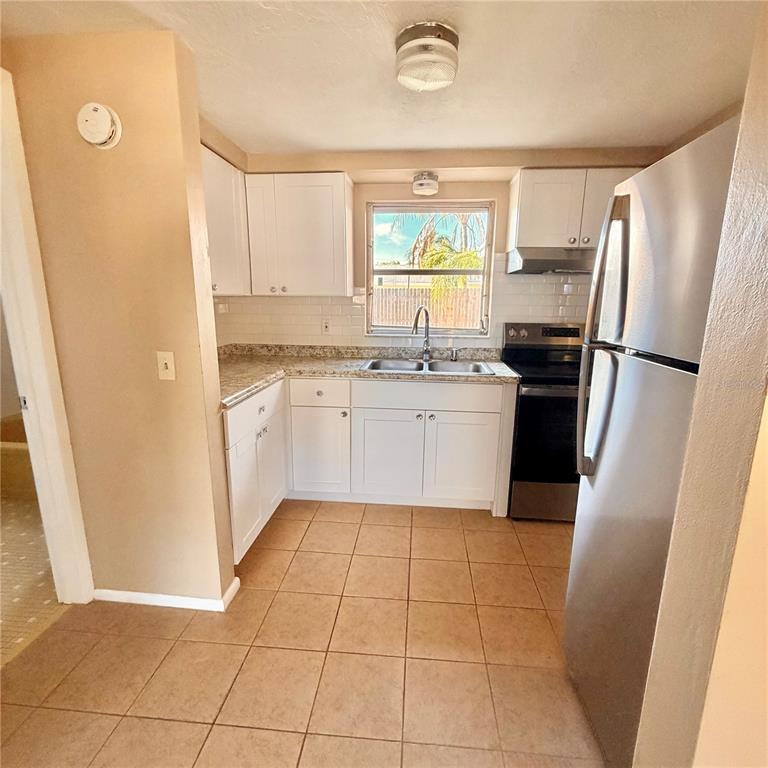 A kitchen features white cabinets, granite countertops, stainless steel appliances, and beige tile flooring — 5401 PASADENA DRIVE, NEW PORT RICHEY, FL