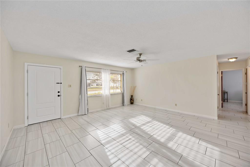An empty living room features light-colored tile flooring, a ceiling fan, and a white door — 181 SANDHURST DRIVE, VENICE, FL