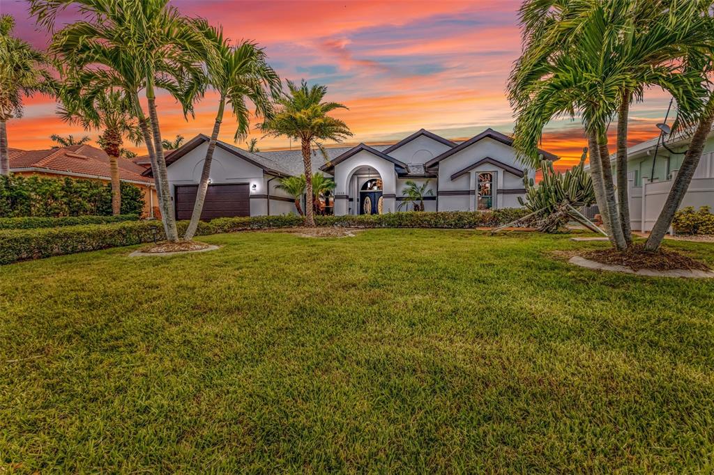 A single-story house with a dark garage door and arched entryway sits behind a lawn — 12558 BACCHUS ROAD, PORT CHARLOTTE, FL