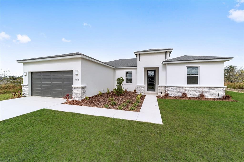 A single-story house with a white stucco exterior, stone accents, and a gray garage door — 16090 SW 42ND TERRACE, OCALA, FL