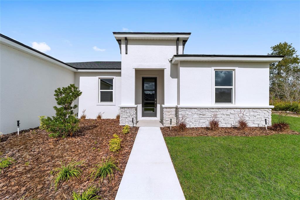 The exterior of a modern white house features a stone-accented entryway and a concrete walkway — 16090 SW 42ND TERRACE, OCALA, FL