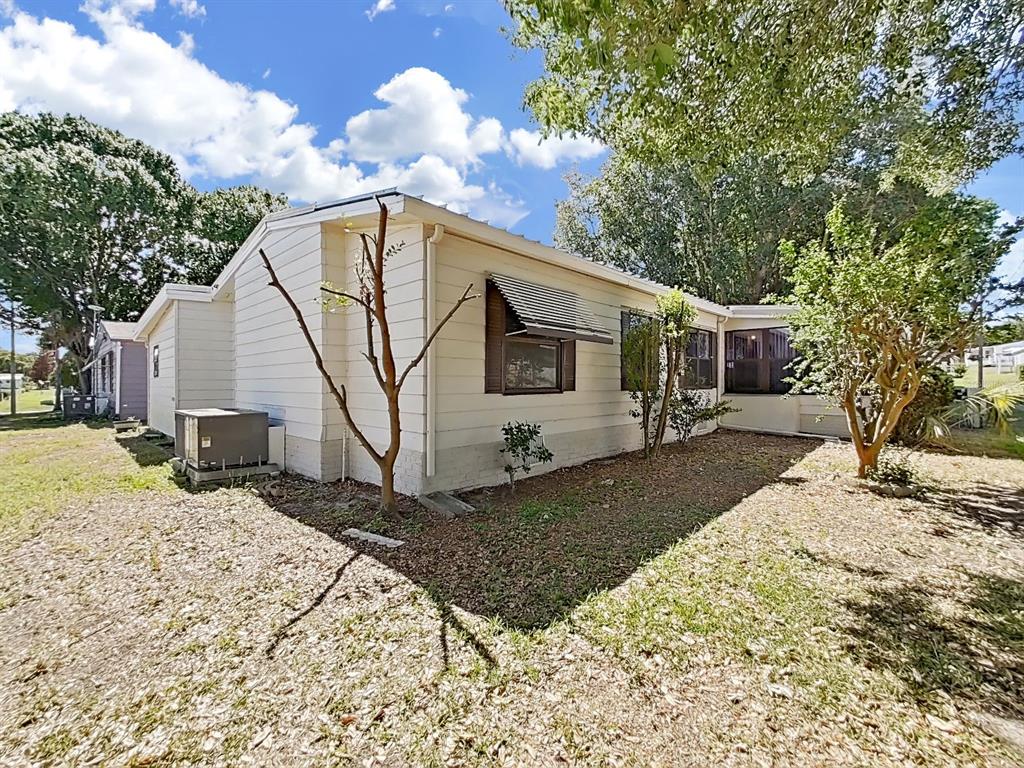 The exterior of a light-colored, single-story house features horizontal siding, an air conditioning unit, and trees — 1688 FOXWAY DR, LAKELAND, FL