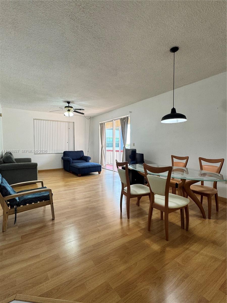 This living and dining area features wood-look flooring, a ceiling fan, and a glass-topped table — 18707 NE 14th Ave # 733, Miami FL 33179, MIAMI, FL