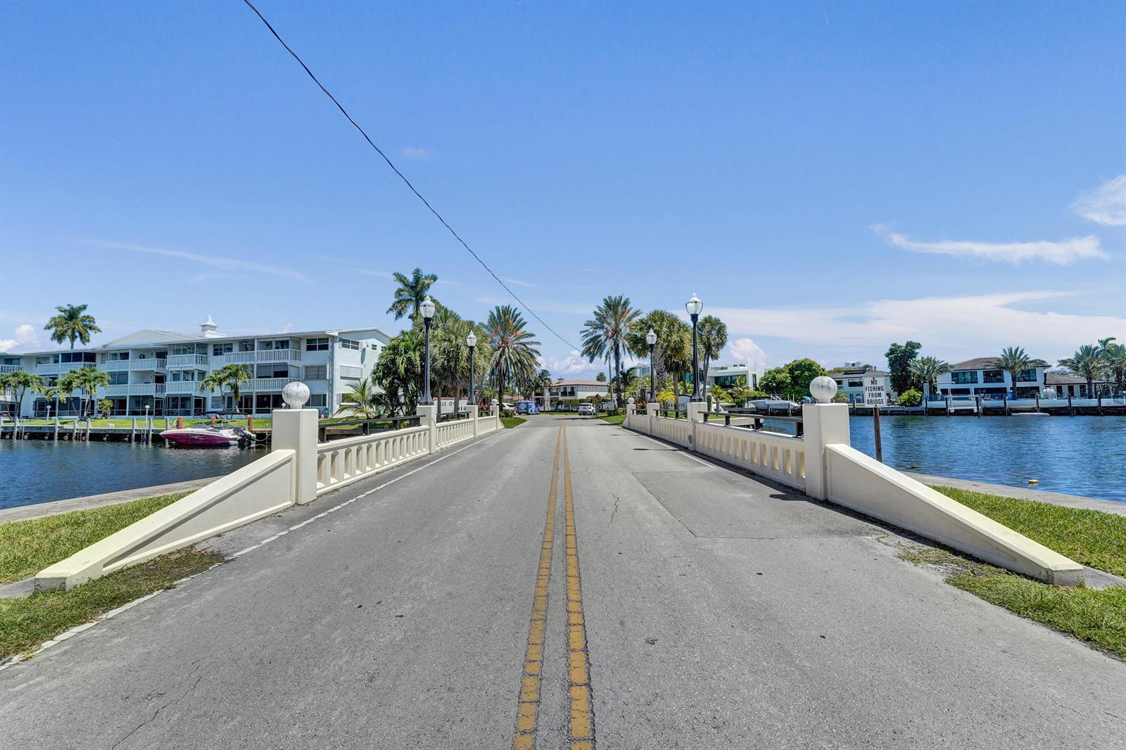 A paved road crosses a bridge over a canal lined with palm trees and buildings — 455 Paradise Isle Boulevard # 305, Hallandale Beach FL 33009, HALLANDALE BEACH, FL