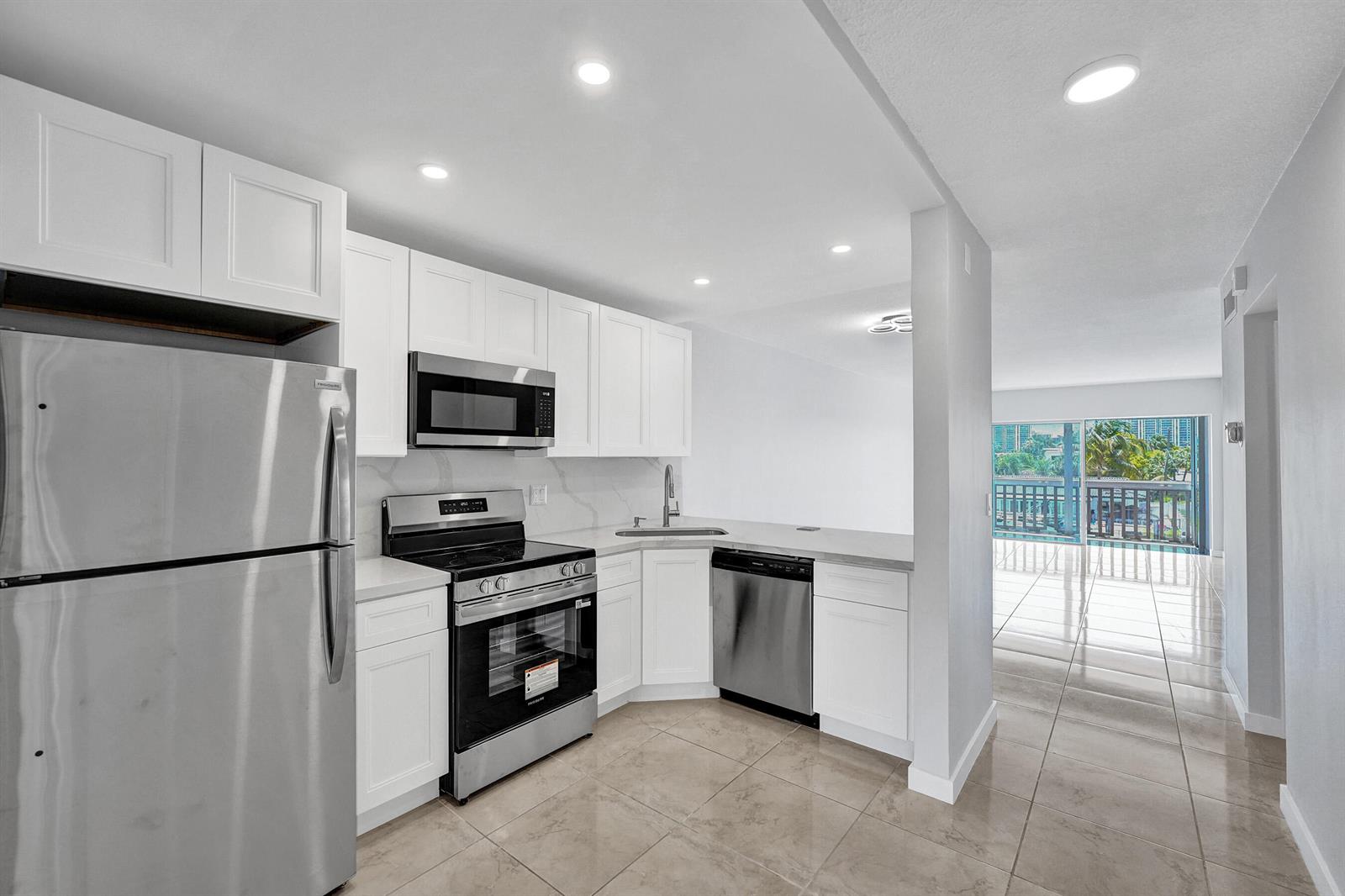 A modern kitchen with white cabinets, stainless steel appliances, and tile flooring — 455 Paradise Isle Boulevard # 305, Hallandale Beach FL 33009, HALLANDALE BEACH, FL