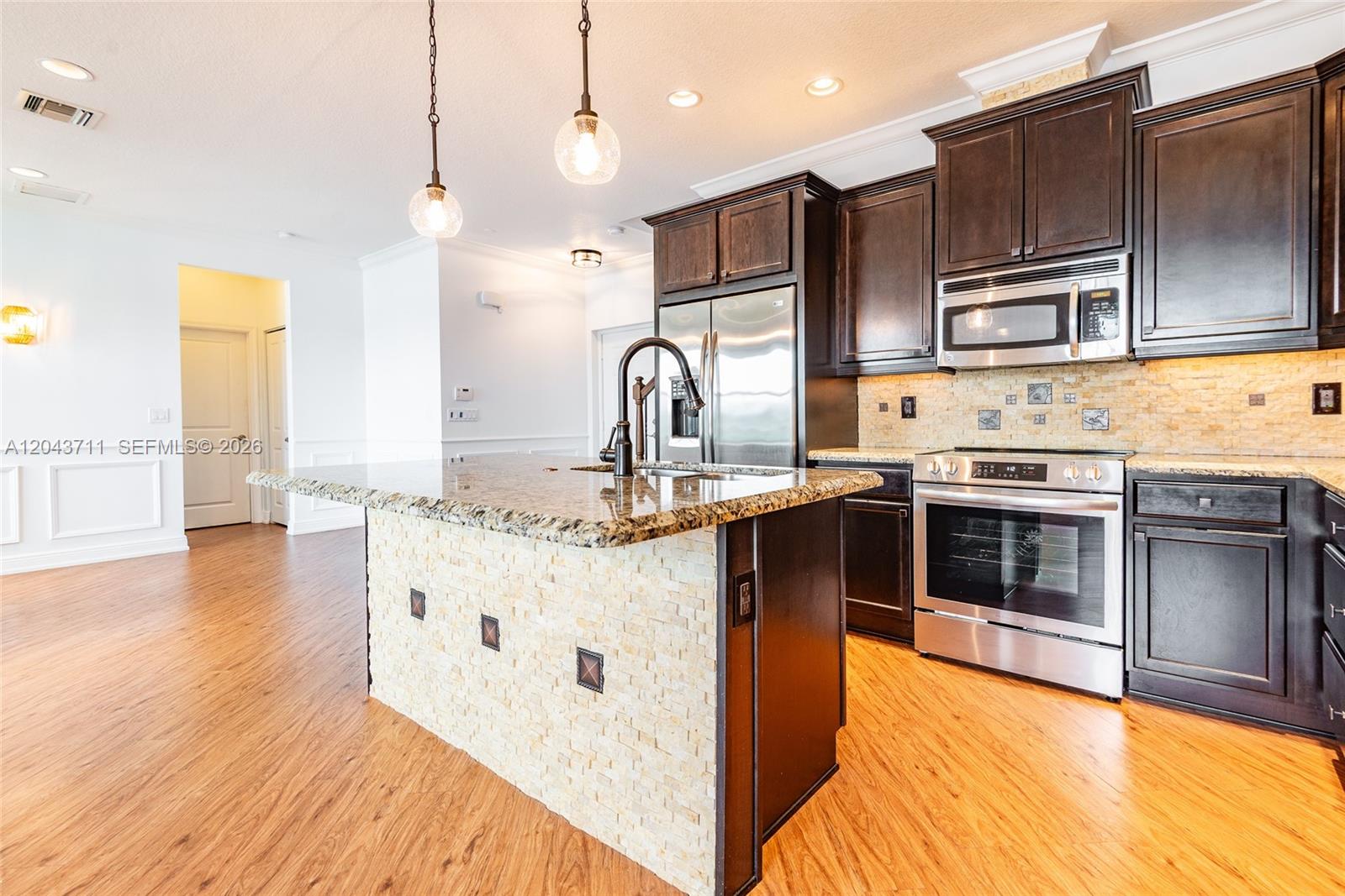 A kitchen features dark wood cabinets, granite countertops, a stone-tiled island, and stainless steel appliances — 3061 Tortola Way, Cooper City FL 33024, COOPER CITY, FL