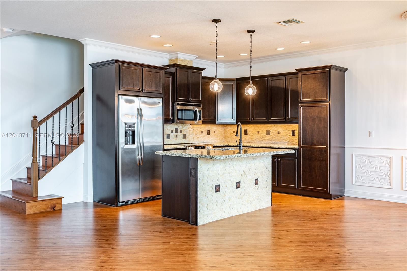 A kitchen features dark wood cabinets, granite countertops, a stone-tiled island, and hardwood flooring — 3061 Tortola Way, Cooper City FL 33024, COOPER CITY, FL