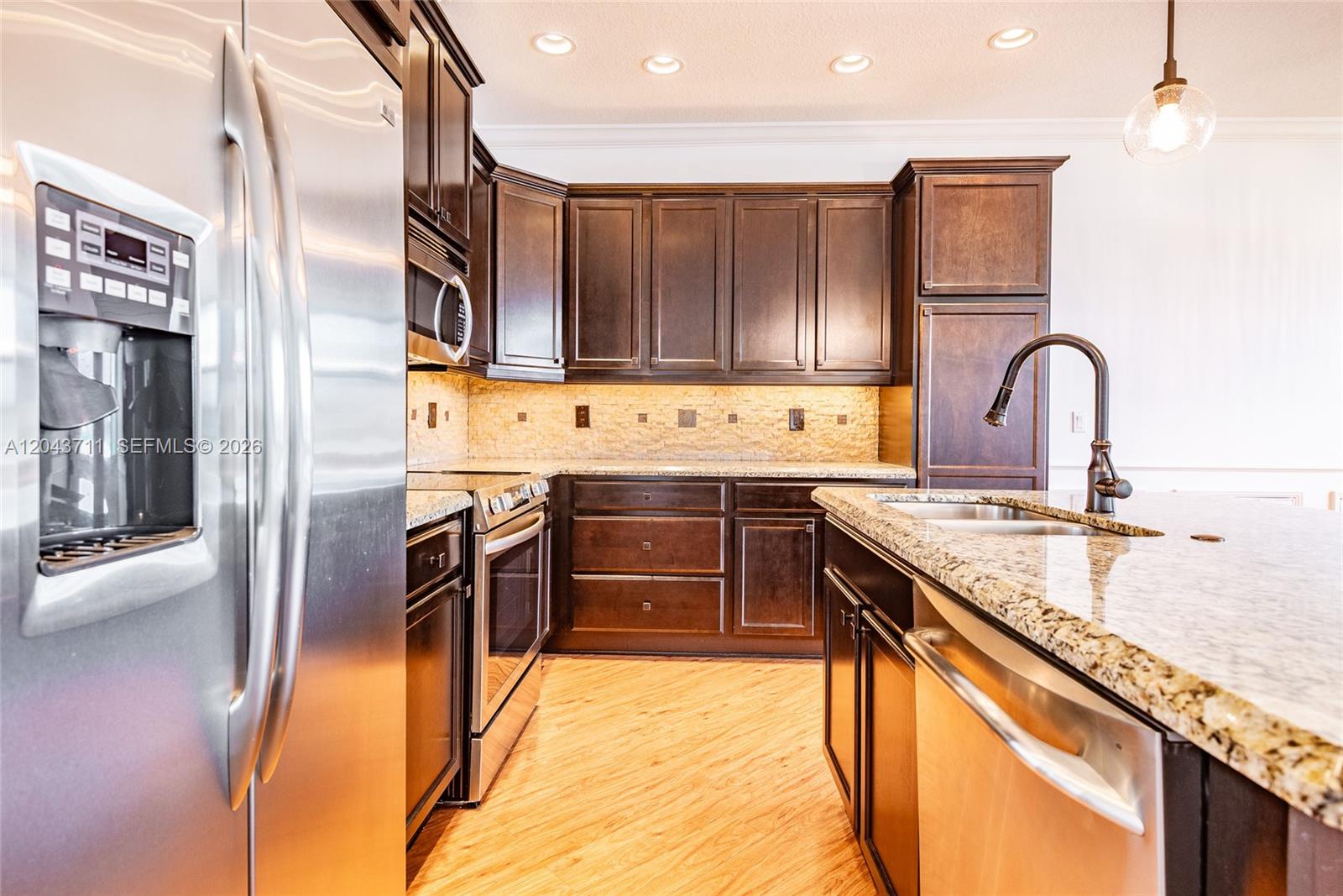 A kitchen features dark wood cabinets, granite countertops, stainless steel appliances, and wood-look flooring — 3061 Tortola Way, Cooper City FL 33024, COOPER CITY, FL