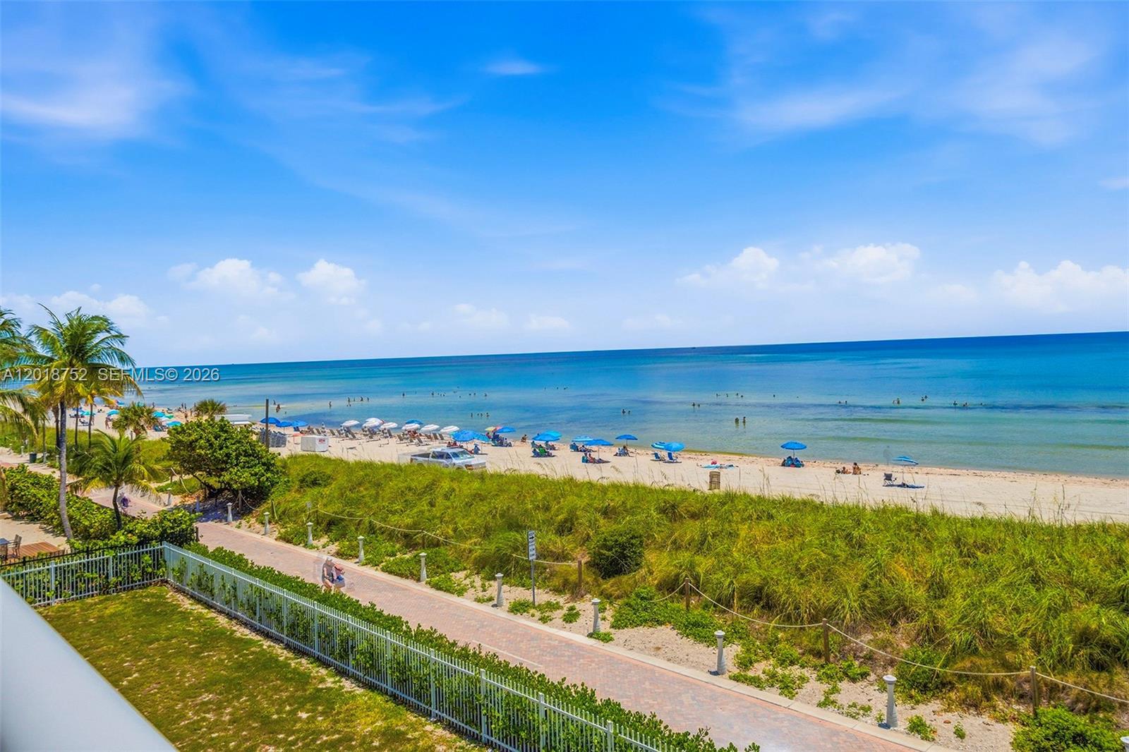 An elevated view of a sandy beach with blue umbrellas and a paved walkway — 5401 Collins Ave # 102, Miami Beach FL 33140, MIAMI BEACH, FL