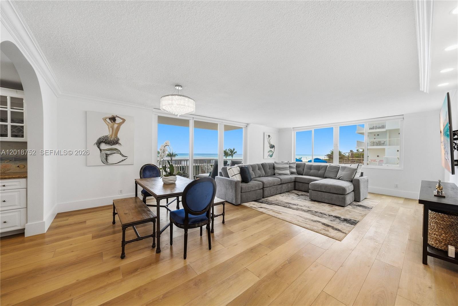 A living and dining area features light wood floors, a gray sectional, and ocean views — 5401 Collins Ave # 102, Miami Beach FL 33140, MIAMI BEACH, FL