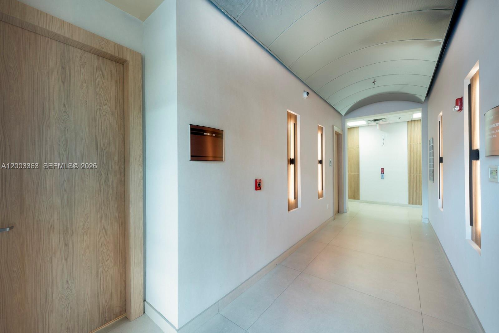 A modern hallway features light wood doors, recessed wall lighting, and a curved ceiling — 6141 Sunset Dr # 110, South Miami FL 33143, SOUTH MIAMI, FL