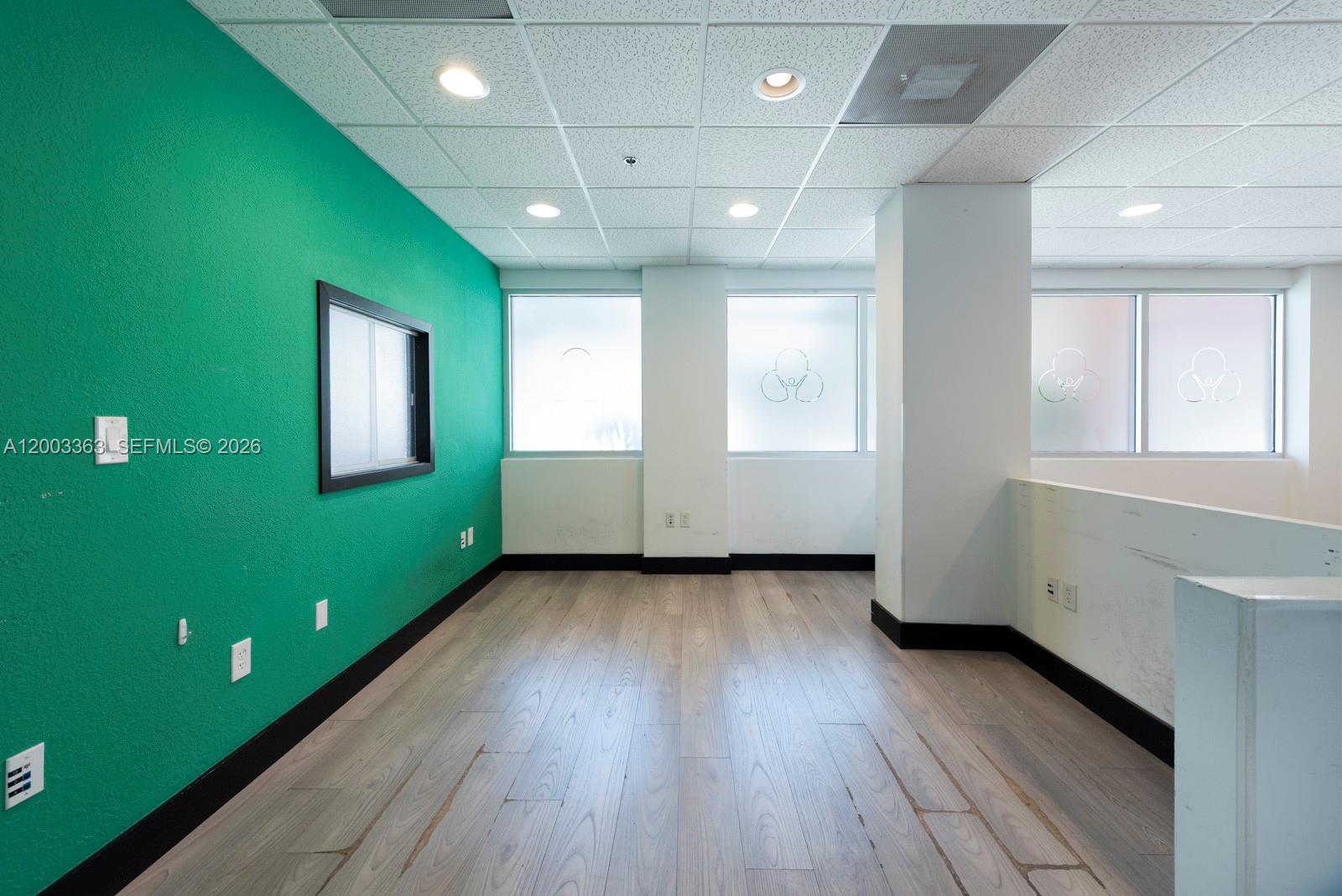 An empty office space features a bright green wall, wood-look flooring, and large windows — 6141 Sunset Dr # 110, South Miami FL 33143, SOUTH MIAMI, FL