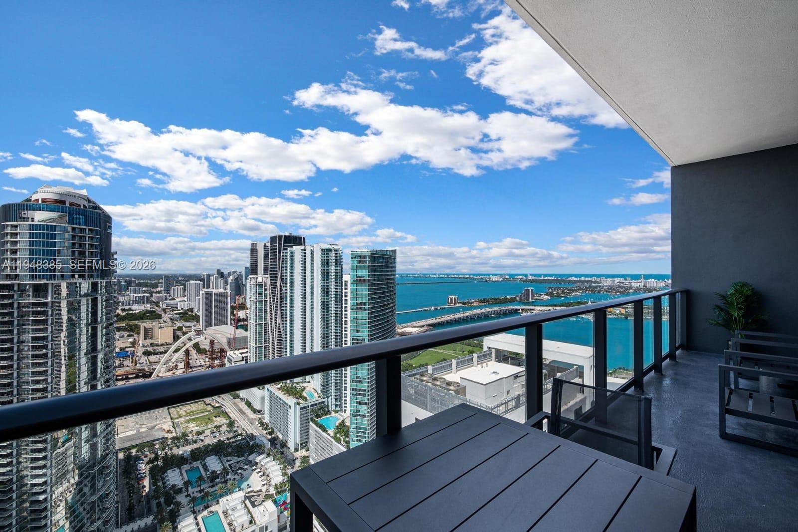 A high-rise balcony overlooks a city skyline, a bridge, and a large body of water — 159 NE 6th St # 5101, Miami FL 33132, MIAMI, FL