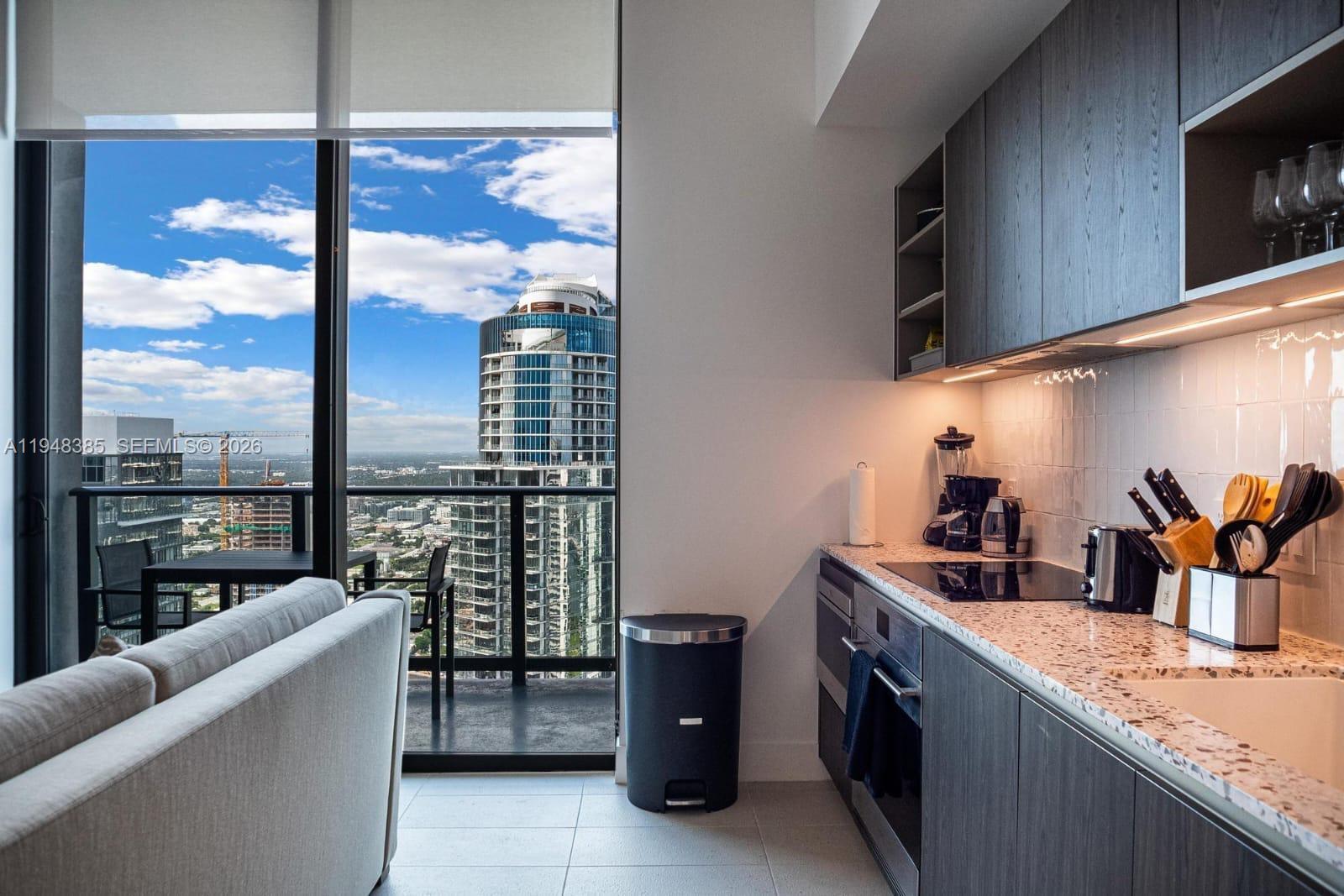 A modern kitchen features dark wood cabinetry, speckled countertops, and a balcony with city views — 159 NE 6th St # 5101, Miami FL 33132, MIAMI, FL