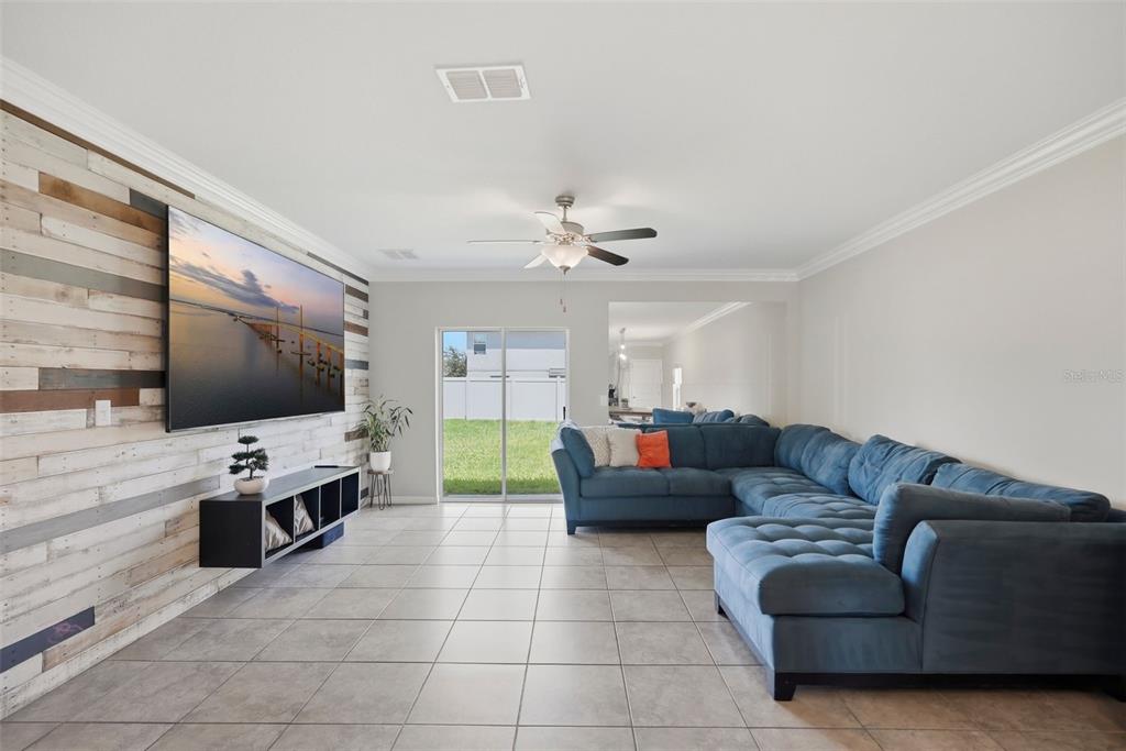 A living room features a blue sectional sofa, a wall-mounted television, and wood-plank accent wall — 17204 YELLOW PINE STREET, WIMAUMA, FL