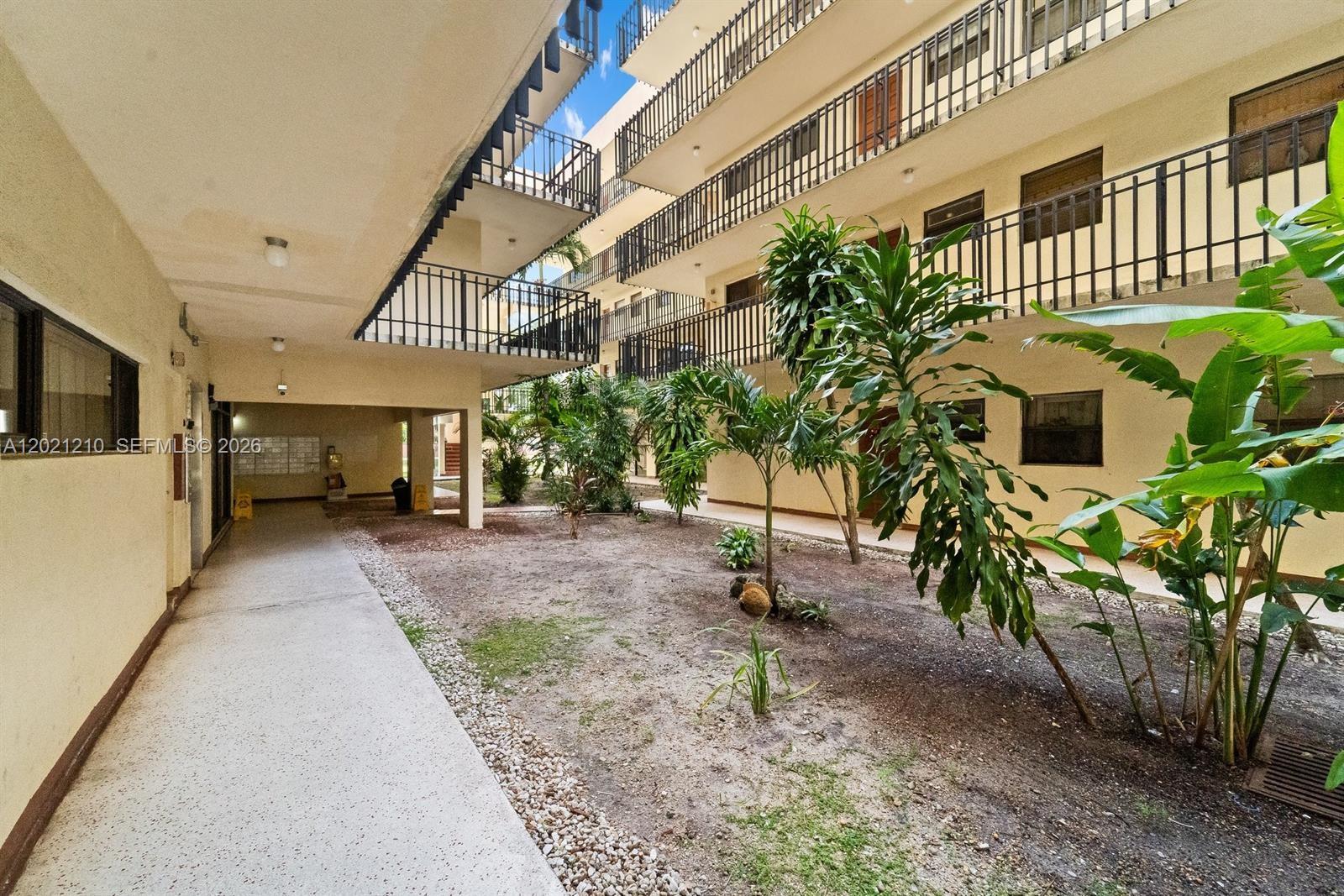 An outdoor courtyard features a concrete walkway, sparse landscaping, and multi-story apartment balconies — 650 NE 149th St # 407A, Miami FL 33161, MIAMI, FL