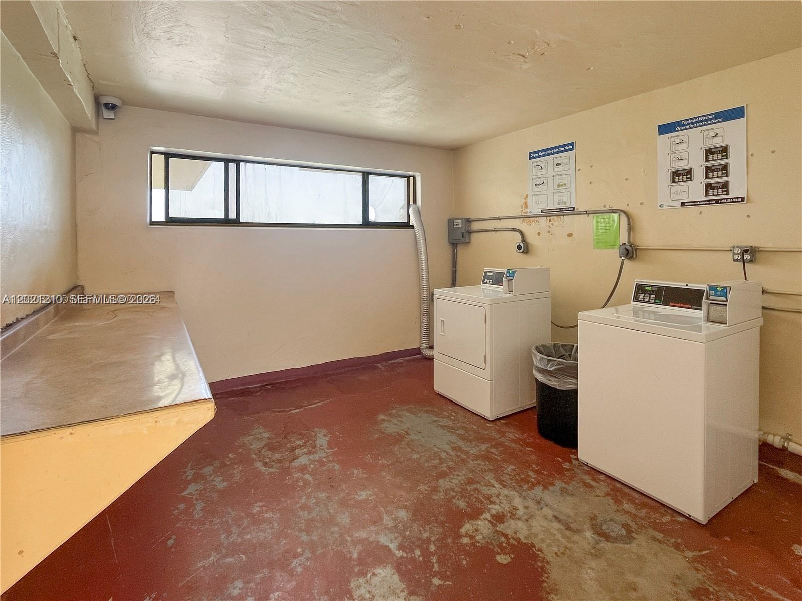 A laundry room features a washer, dryer, folding counter, and a window on a red floor — 650 NE 149th St # 407A, Miami FL 33161, MIAMI, FL