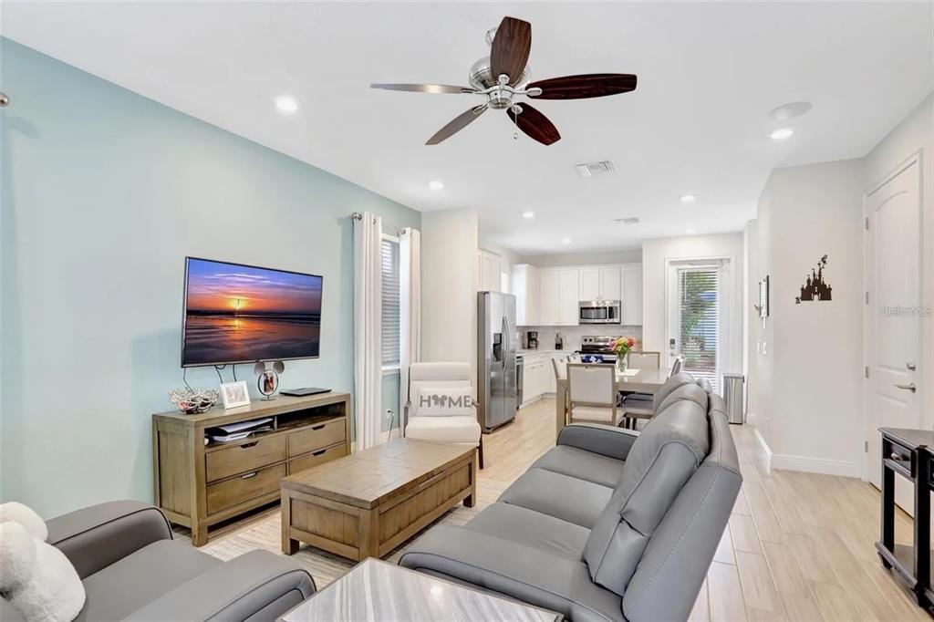 An open-concept living room features a light blue wall, gray sofa, and kitchen beyond — 8044 LOST SHAKER LANE, KISSIMMEE, FL