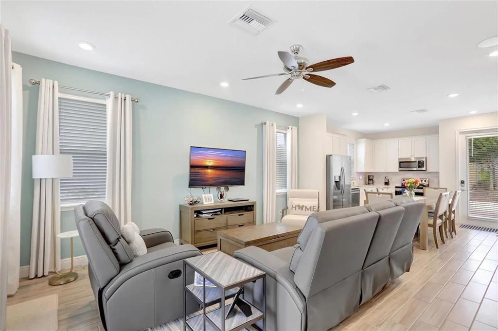A living room with gray furniture, a television, and an open-concept kitchen with white cabinets — 8044 LOST SHAKER LANE, KISSIMMEE, FL