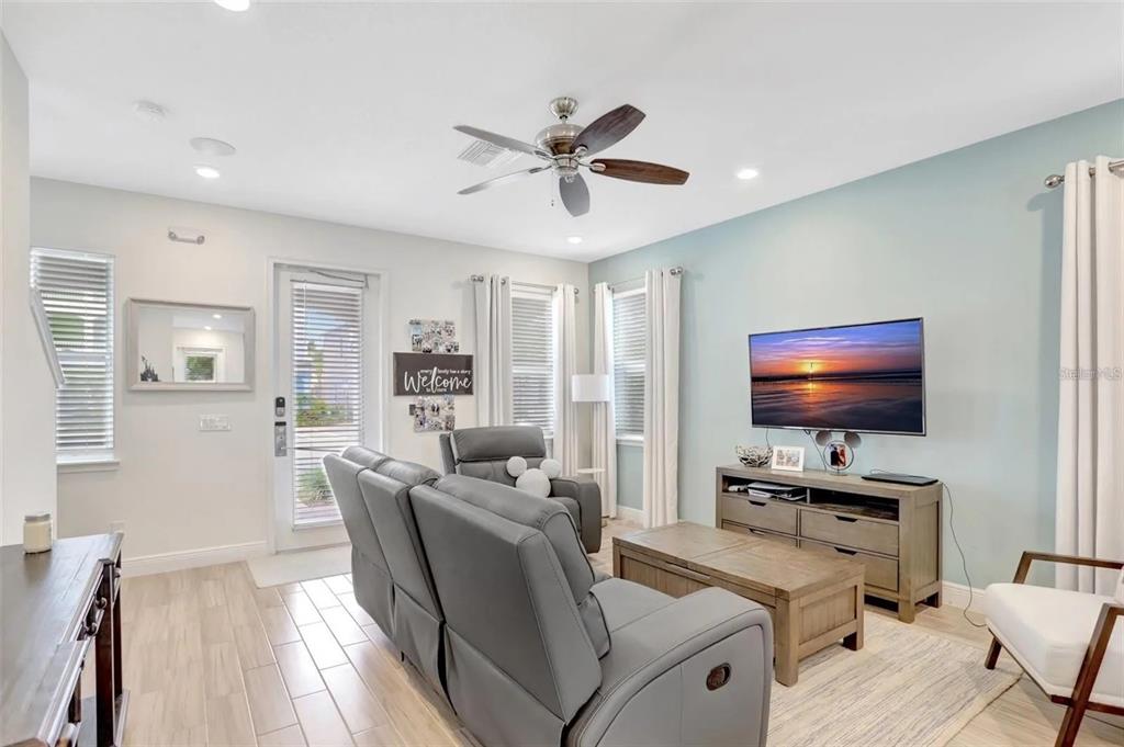A living room features gray reclining furniture, a wooden coffee table, and a wall-mounted television — 8044 LOST SHAKER LANE, KISSIMMEE, FL