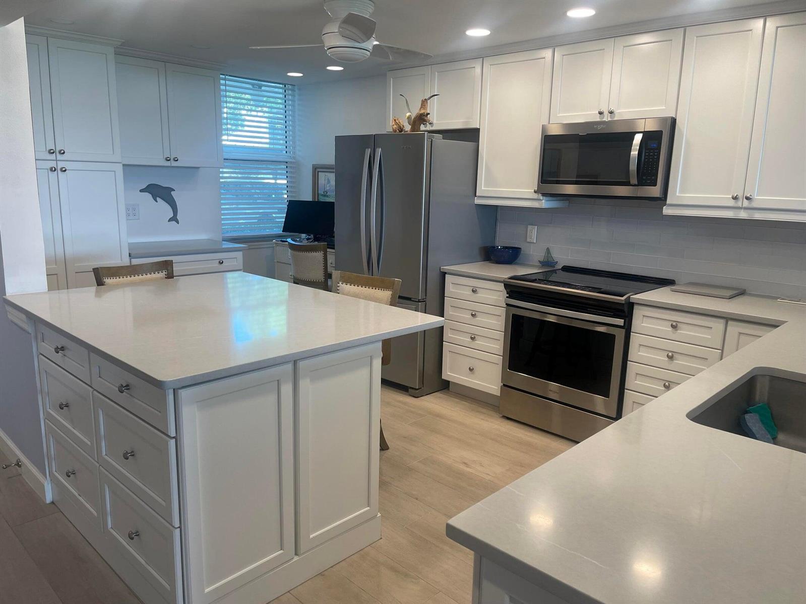 A modern kitchen features white cabinetry, stainless steel appliances, a large island, and quartz countertops — 1950 SW Palm City Road # 13104, Stuart FL 34994, STUART, FL
