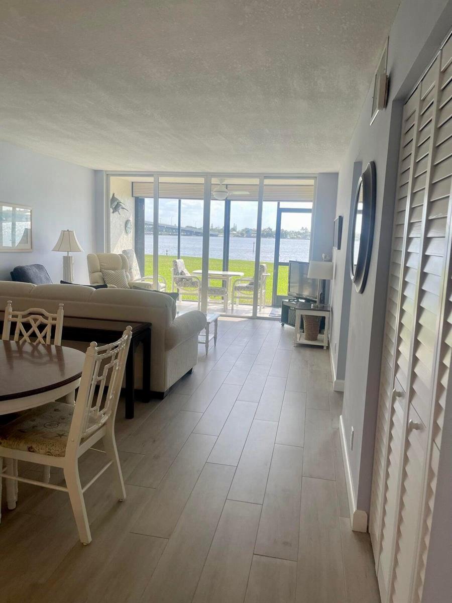 A living room with light wood-look tile floors leads to a patio overlooking the water — 1950 SW Palm City Road # 13104, Stuart FL 34994, STUART, FL